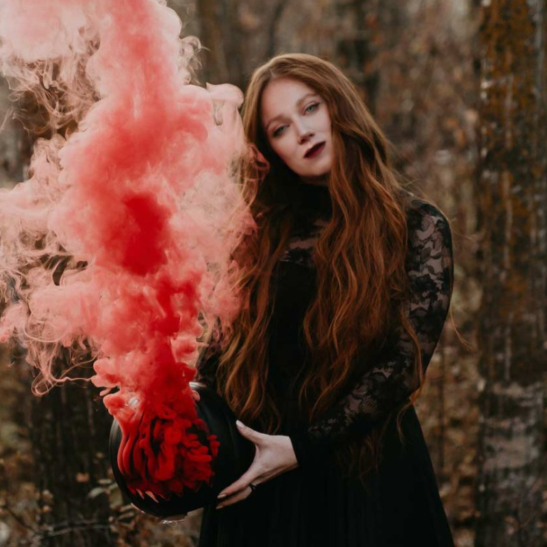 Jessica wears a spooky black dress and holds a black pumpkin that's billowing red smoke from its mouth.